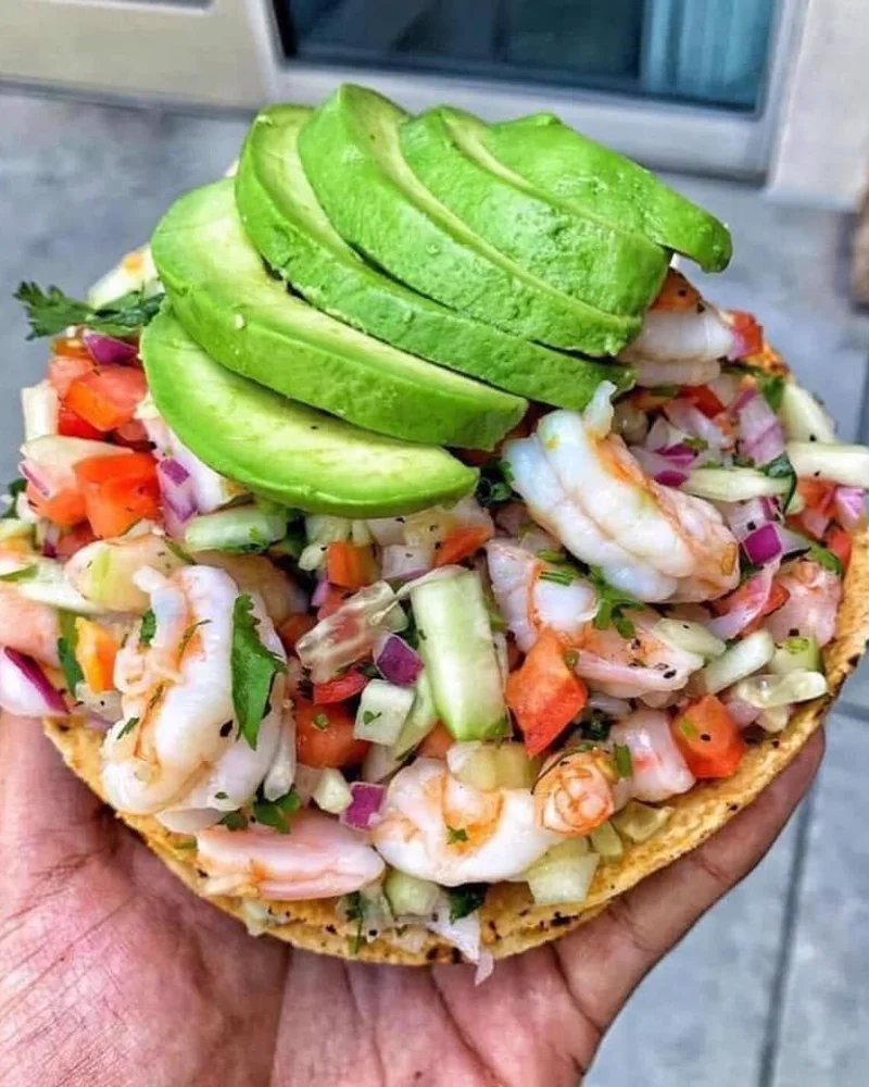 A shrimp tostada with avocado held in hand
