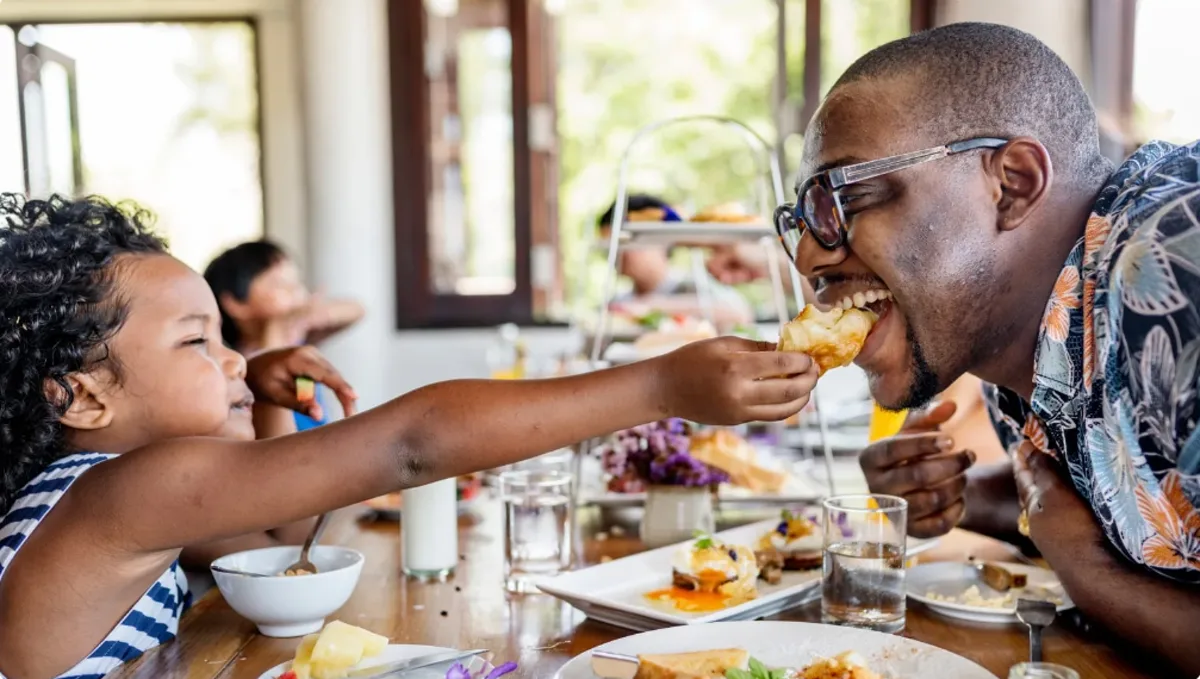 A child sharing a bite with a guest across the villa table